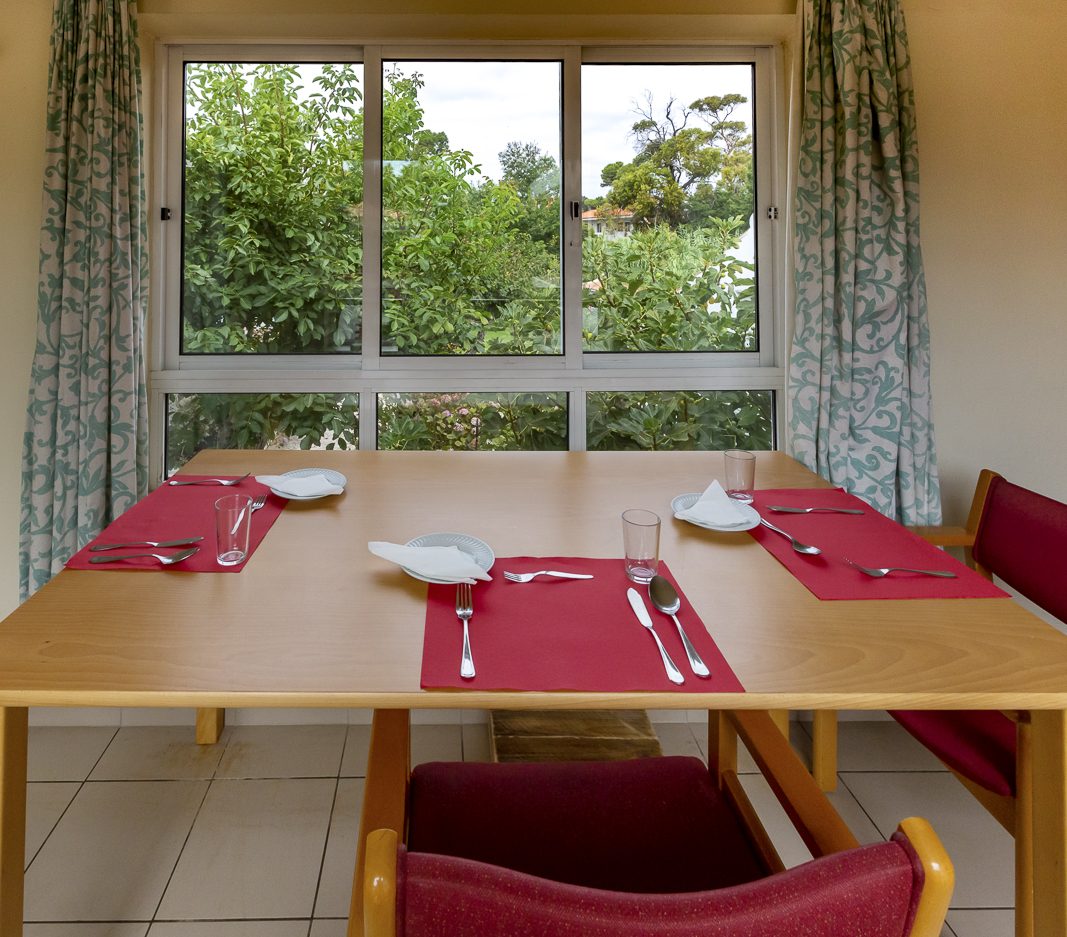A dining table laid for lunch beside a window looking onto the trees