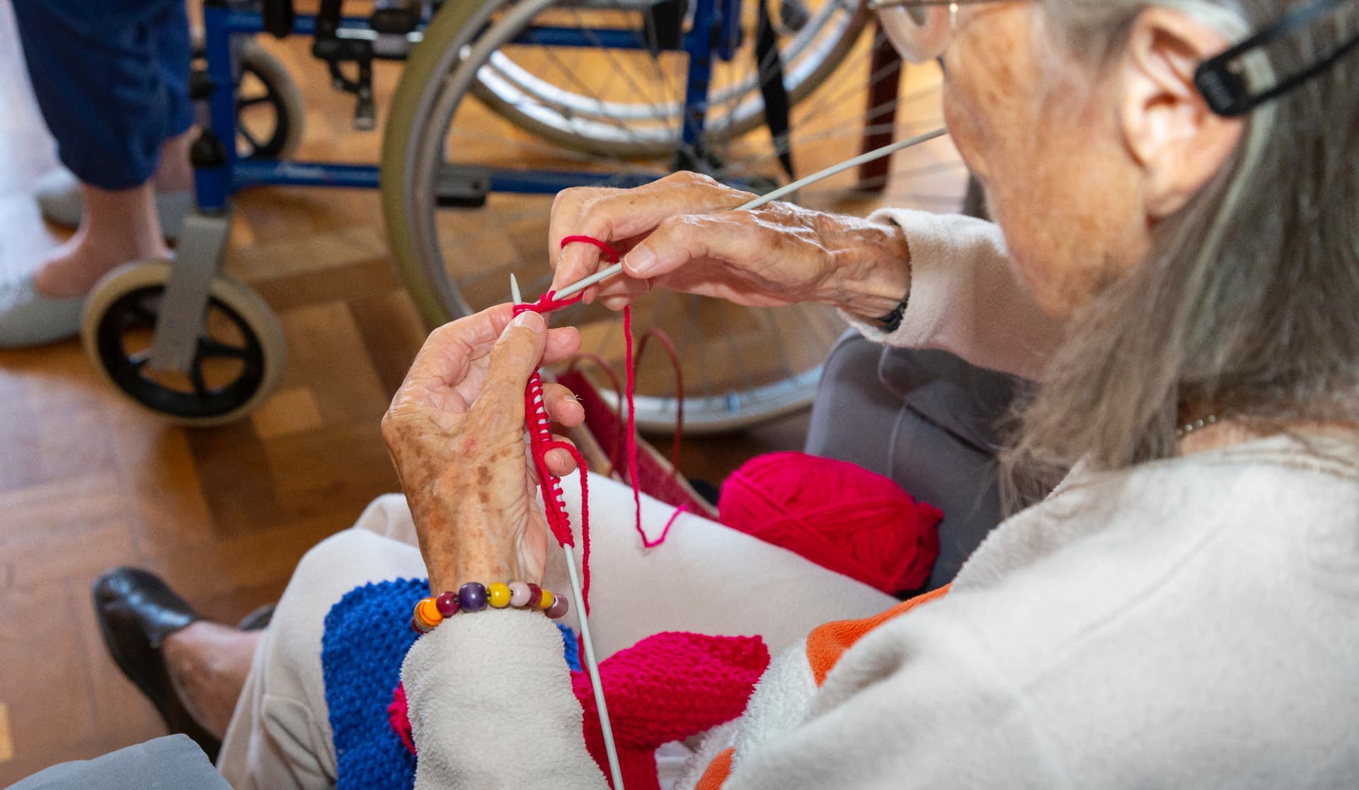 A resident knitting with bright pink wool in the lounge
